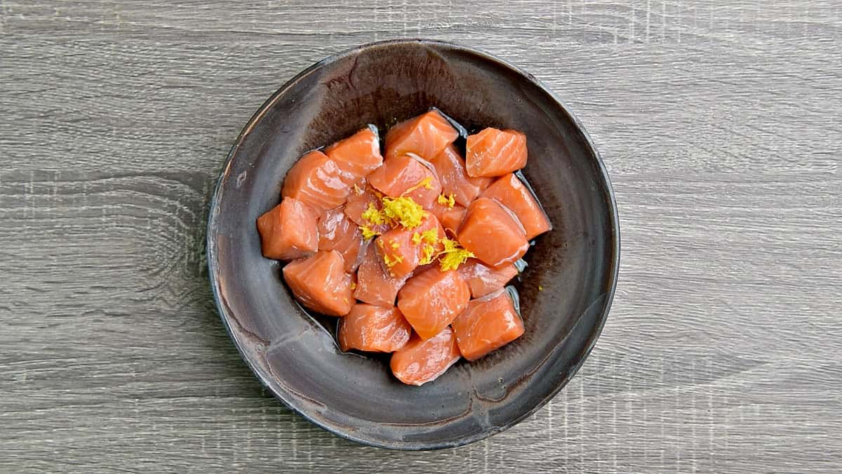Salmon pieces in a bowl with lemon zest and oil.