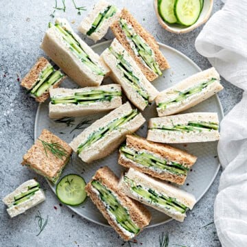 Top down view of a dozen cucumber and cream cheese finger sandwiches laying all different directions on a large gray plate.