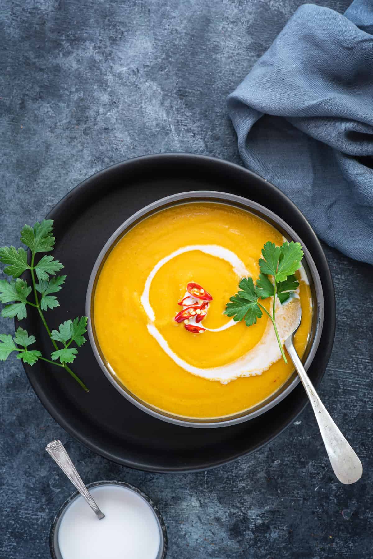 A bowl of pumpkin curry soup with herbs, red chili peppers for garnish, and coconut milk drizzled on top. 