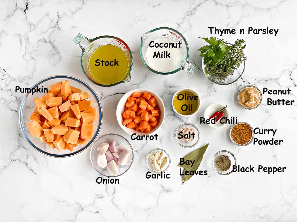 The ingredients to make soup in individual bowls, including pumpkin, stock, coconut milk, herbs, onion, garlic, carrot, olive oil, curry powder, peanut butter, and seasonings.