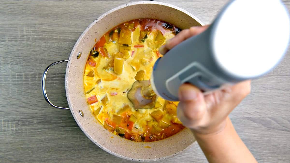 An immersion blender blending the soup in the pot. 