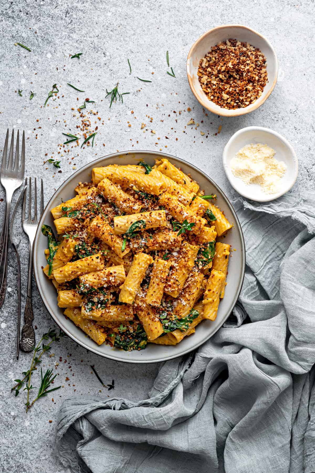 A bowl of pumpkin pasta with spinach, parmesan, and red pepper flakes in bowls on the side.