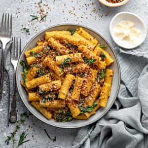 A bowl of creamy pumpkin pasta with spinach, parmesan, and red pepper flakes in bowls on the side.