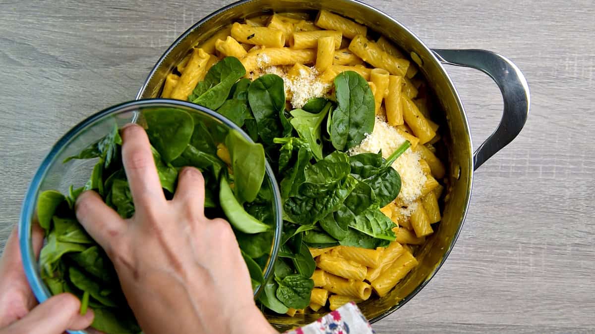 Adding parmesan cheese and fresh spinach to the pot of pumpkin pasta. 