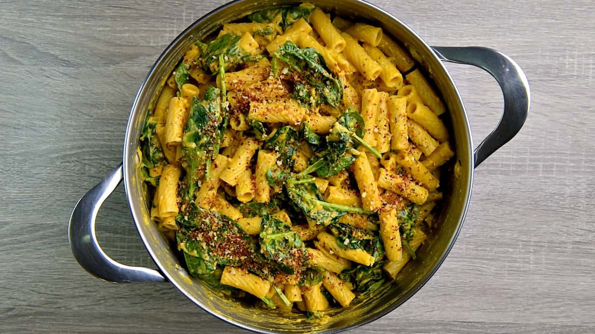 A pot full of pumpkin pasta with spinach, herbs, and toasted panko breadcrumbs sprinkled on top. 