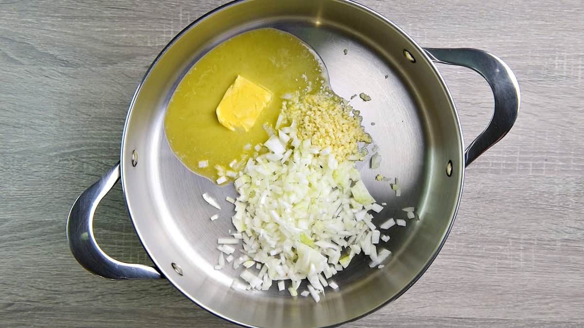 Butter cooking with onion and garlic in a pot.