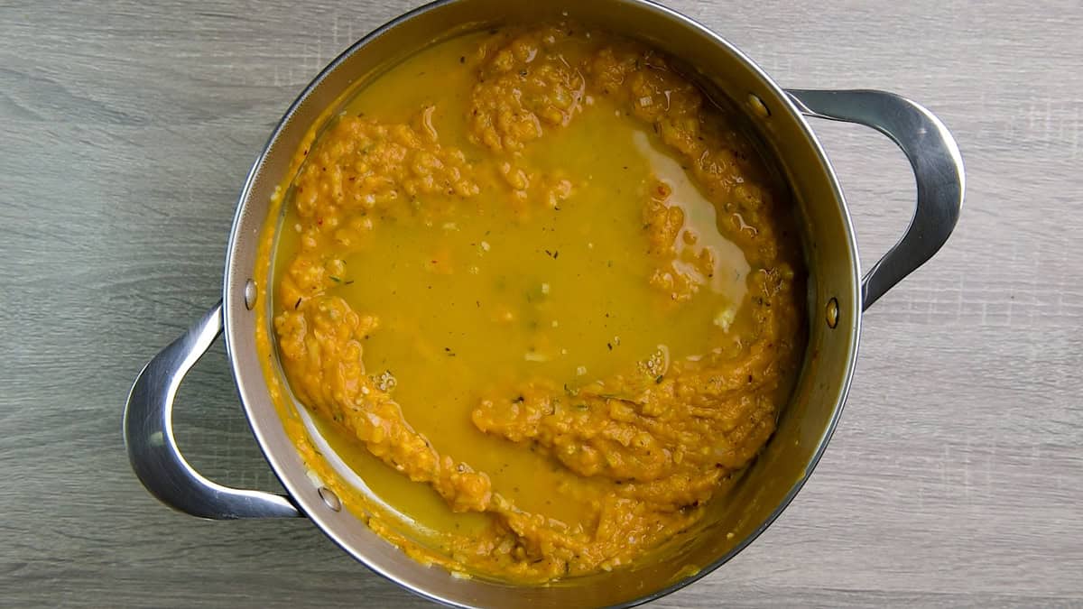 Pumpkin puree, herbs, and vegetable stock cooking in a pot. 