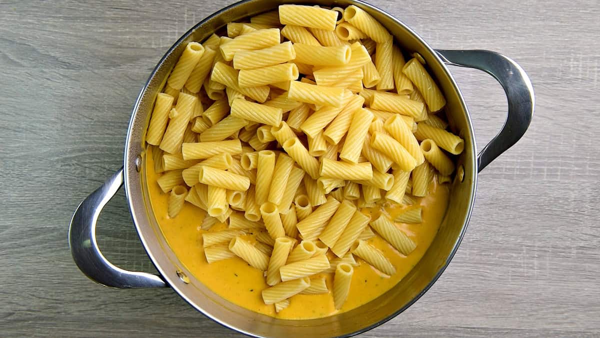 Adding cooked pasta to the creamy pumpkin sauce.