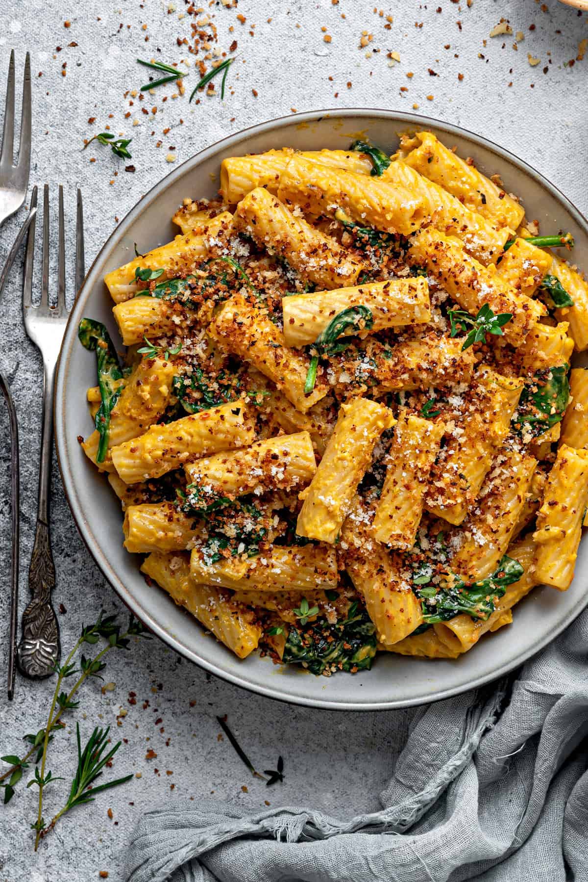 An overhead close-up of pasta in creamy pumpkin sauce, topped with toasted panko breadcrumbs and fresh herbs. 