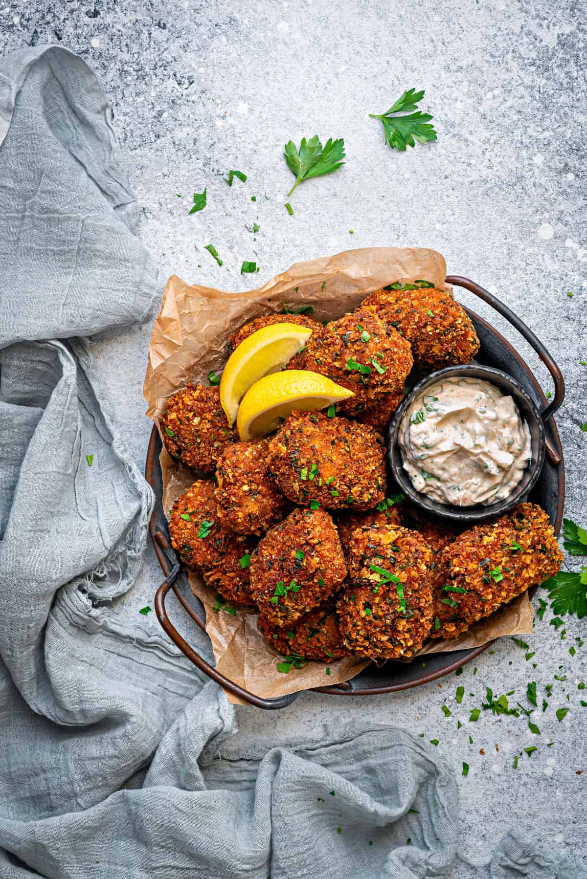 A dish full of fish nuggets served alongside lemon wedges and a sauce in a bowl.