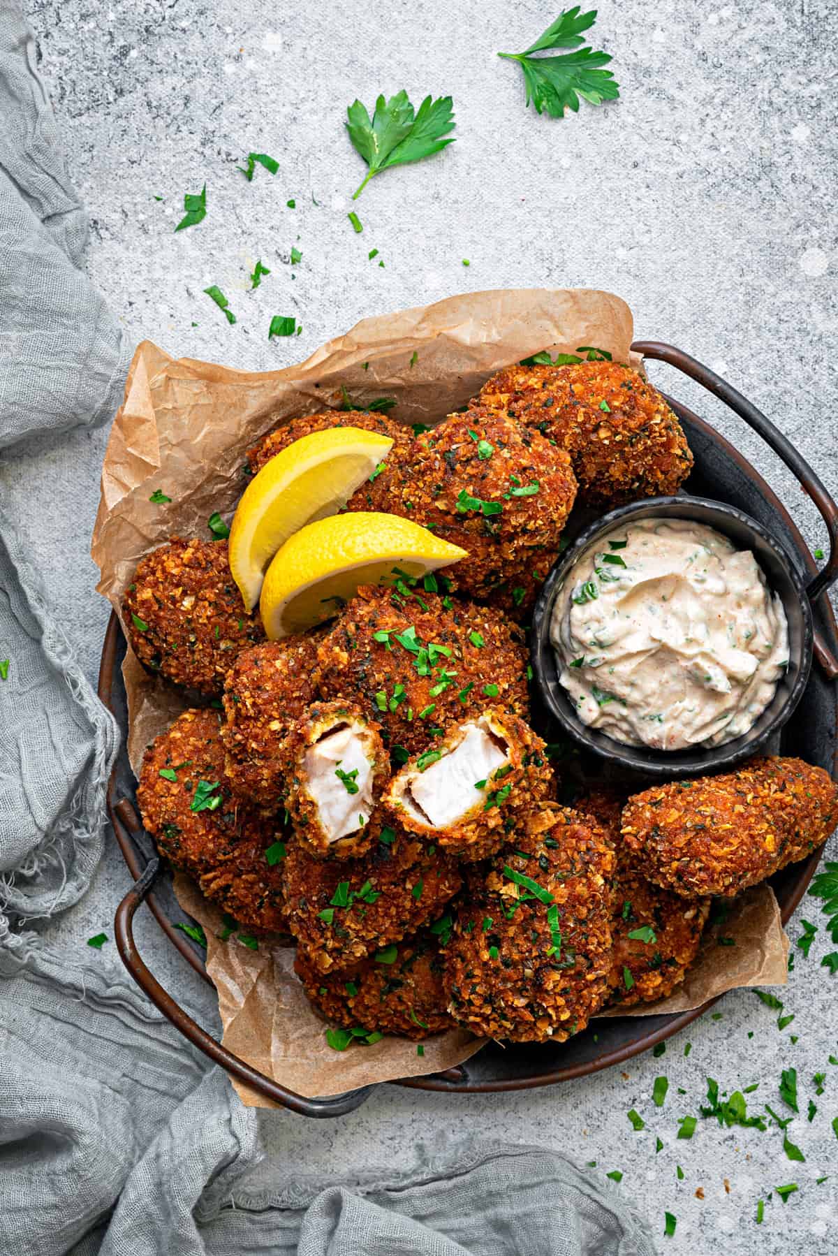 A close-up of fish nuggets in a parchment lined bowl with lemon wedges and a dipping sauce.