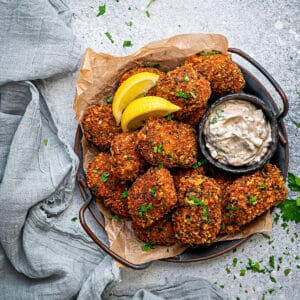 A dish full of fish nuggets served alongside lemon wedges and a sauce in a bowl.