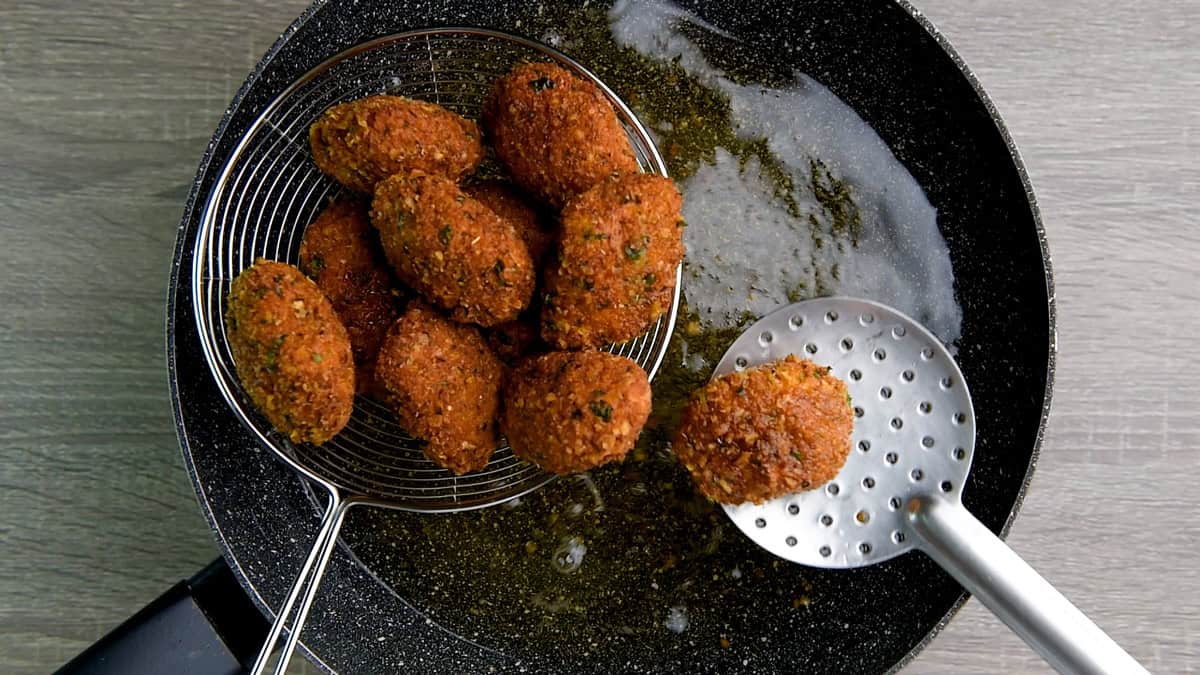 Removing the fried fish nugget  from the oil with a slotted spoon.