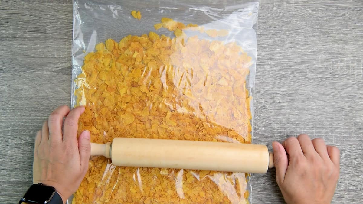 Crushing cornflakes in a ziplock using a rolling pin.