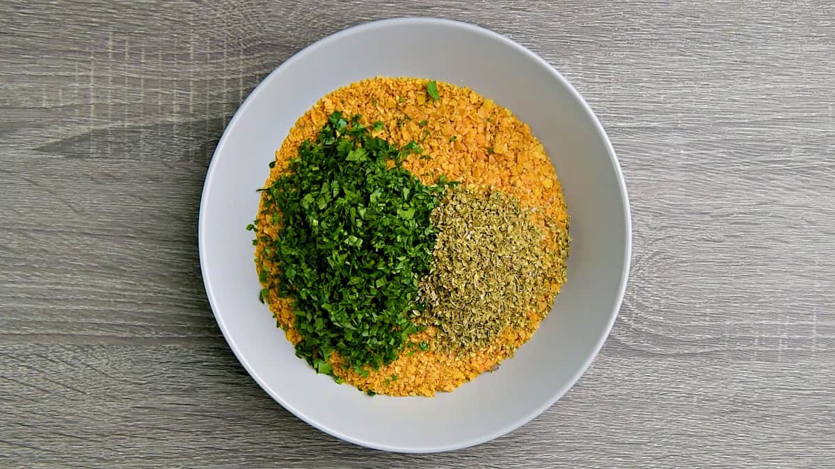 Add fresh parsley herb and dried oregano to crushed cornflakes.